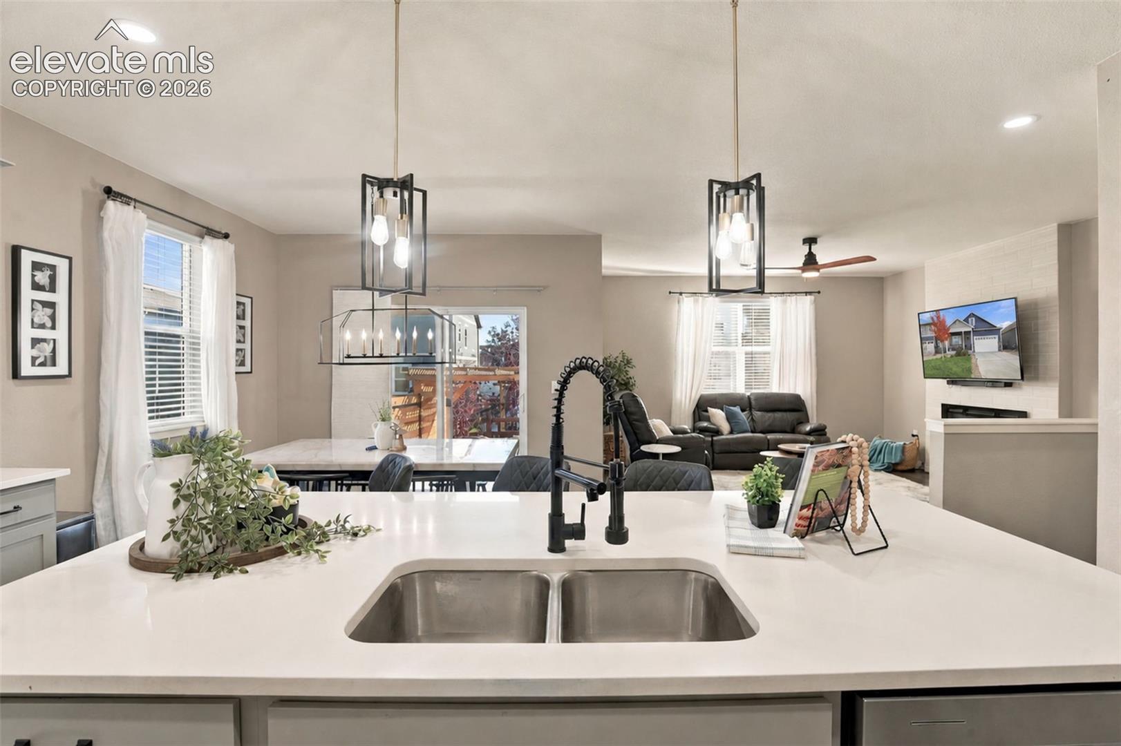 Kitchen island featuring a solid surface countertop, dual-basin stainless steel sink, and high-arch matte black faucet, illuminated by geometric pendant lighting