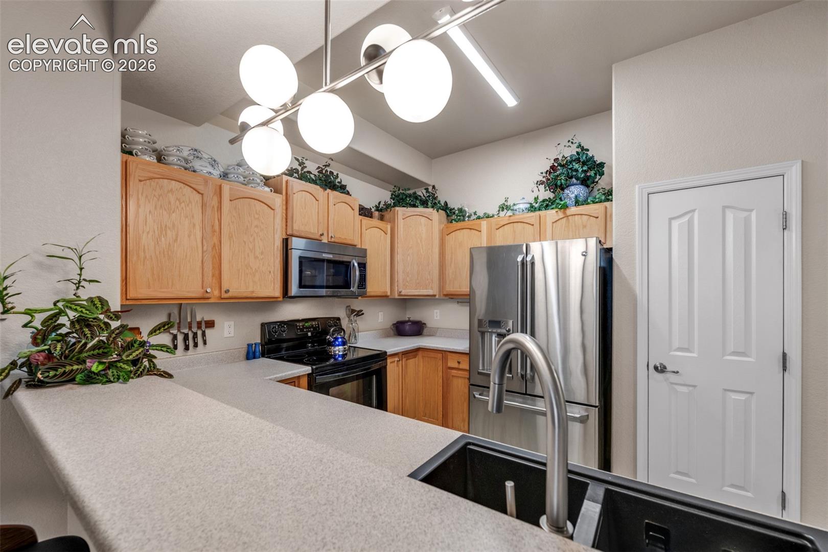 Kitchen featuring light wood cabinetry, white countertops, built-in stainless steel microwave, black electric range, and a stainless steel refrigerator
