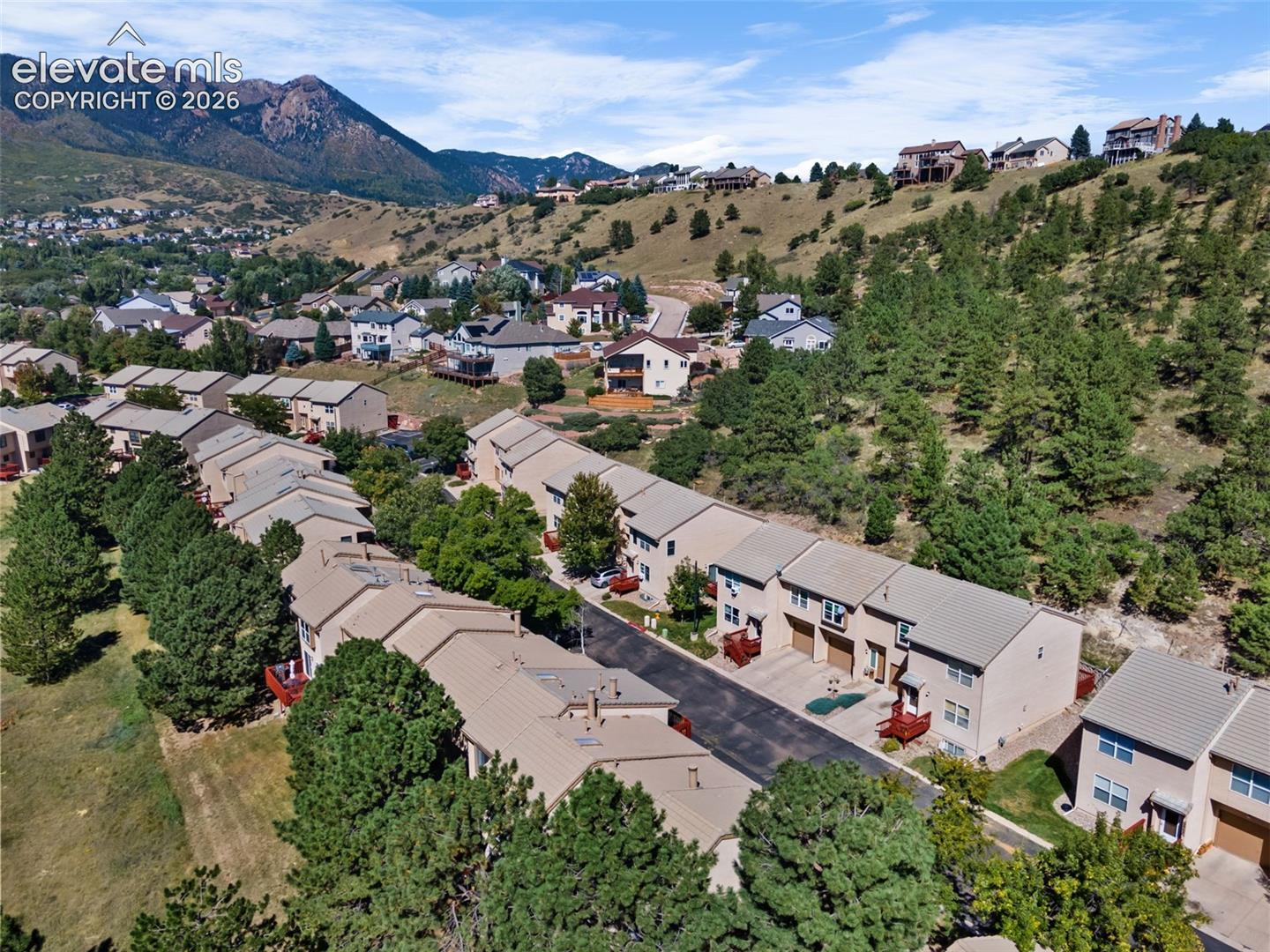 Aerial perspective featuring multi-story structures, asphalt driveways, and proximity to mountainous terrain and evergreen vegetation