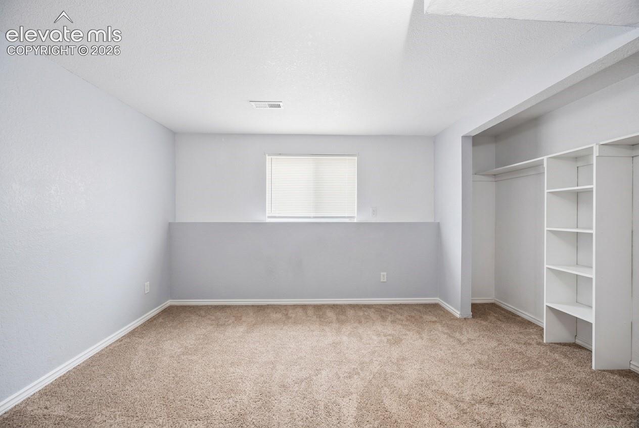 Recessed window with privacy blind, carpeted flooring, and built-in shelving with hanging rod
