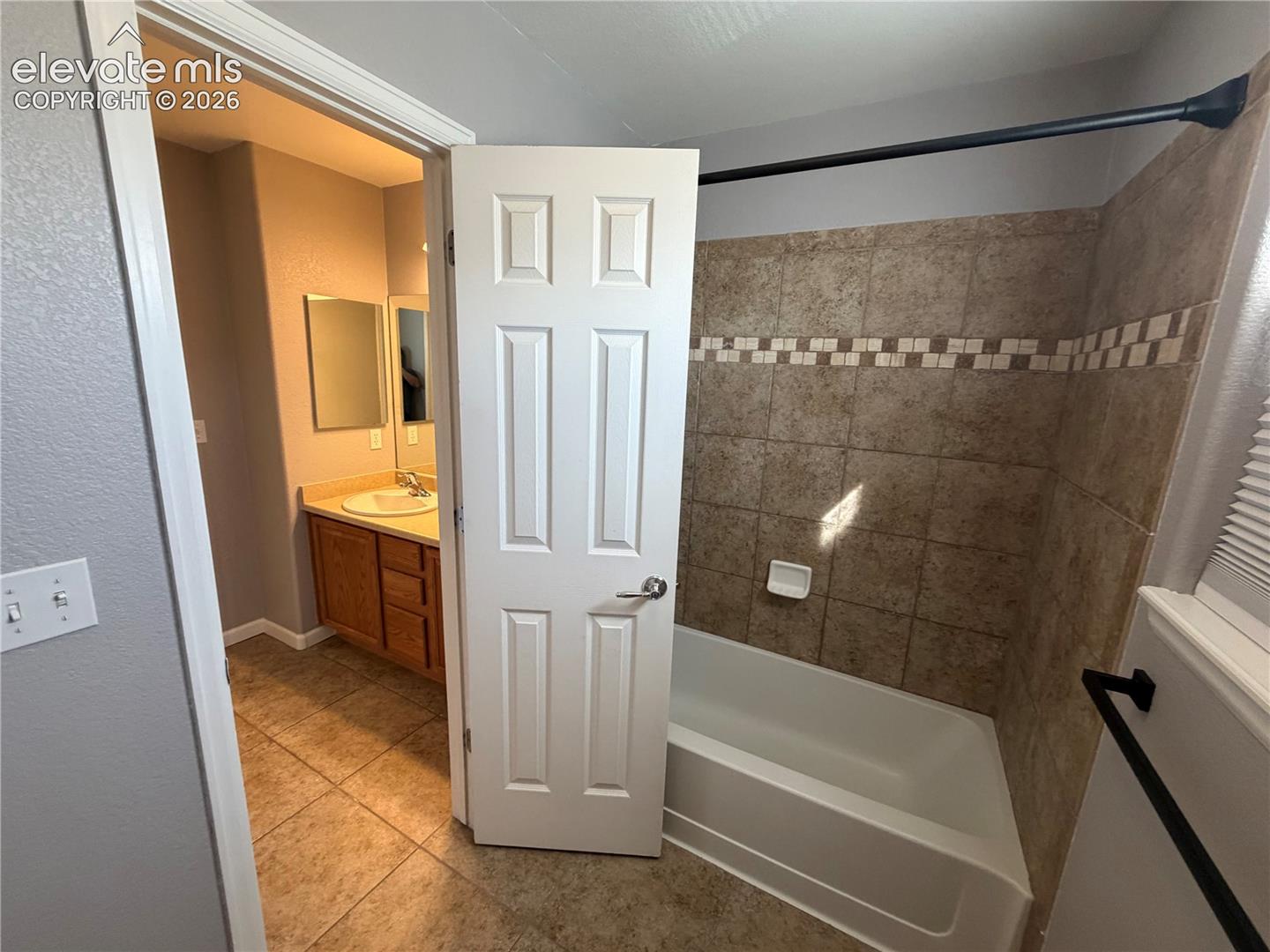 Bathtub with tile surround, decorative mosaic tile accent, and a single-pane window
