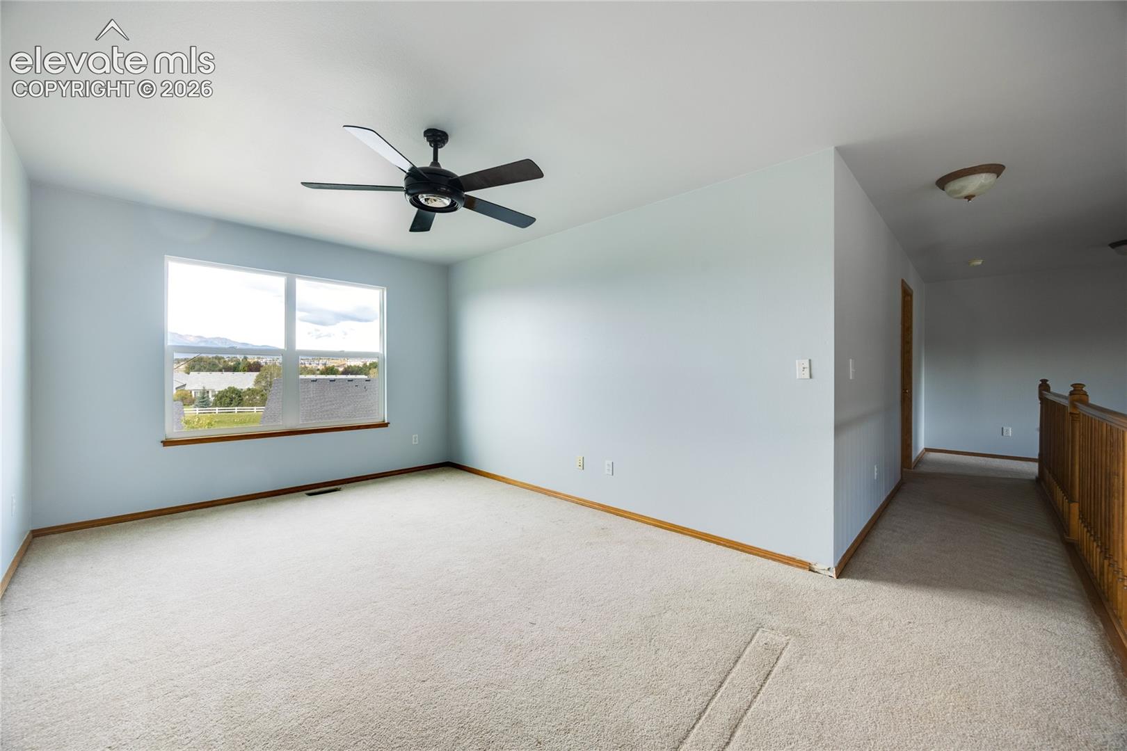 Carpeted room with a ceiling fan, a large window, and a wooden railing