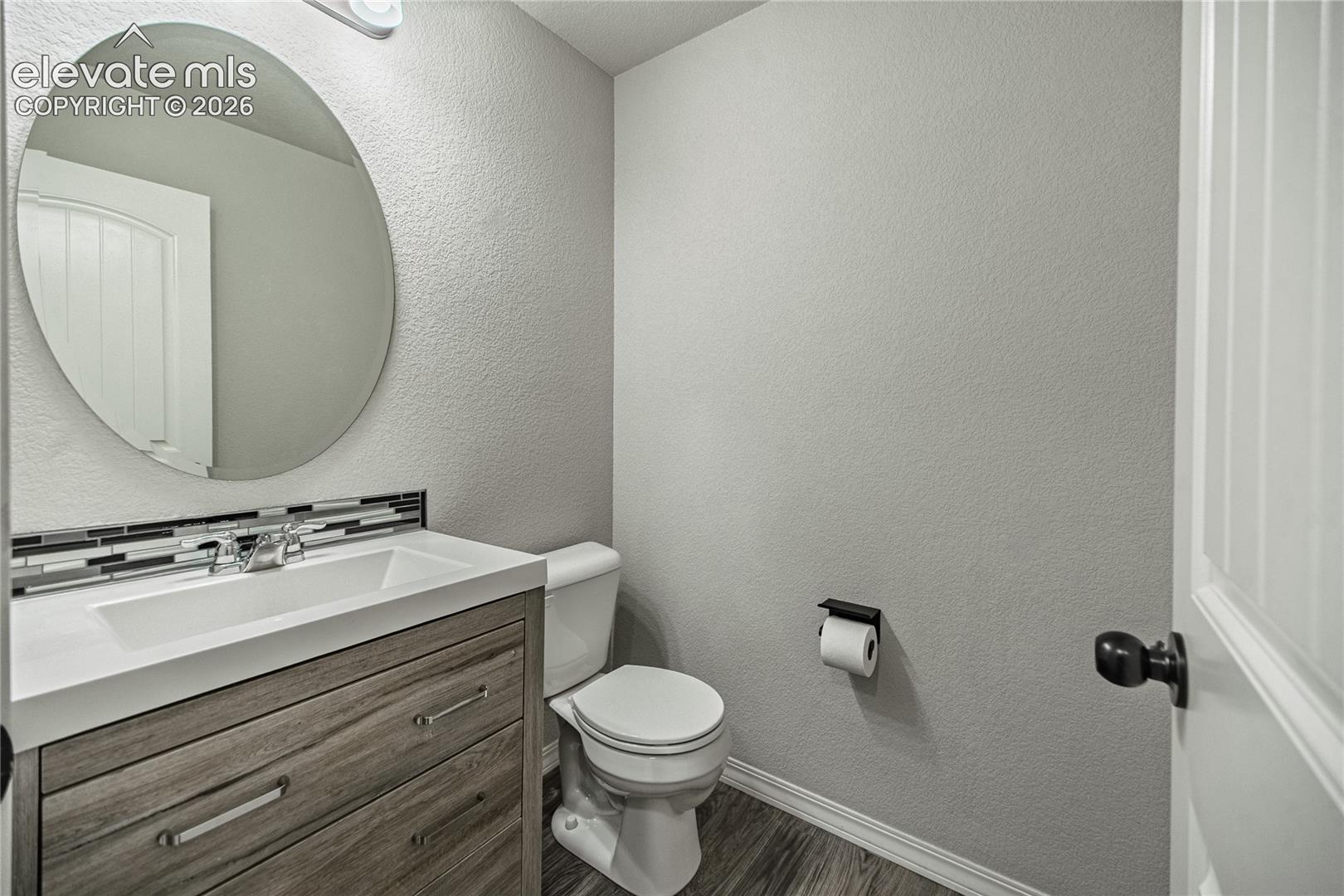 Contemporary vanity with wood-finish cabinetry, integrated sink, and mosaic tile backsplash