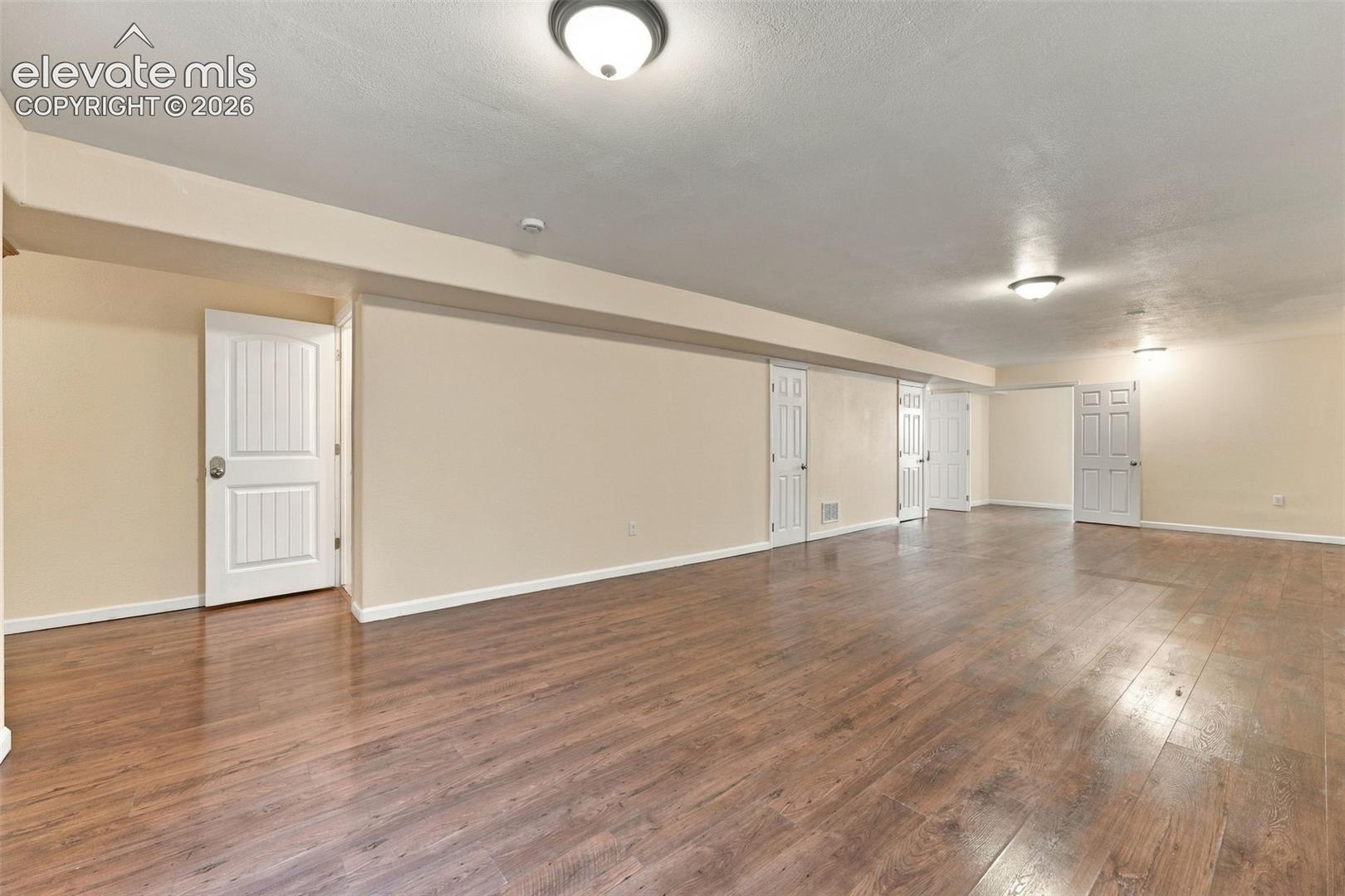 Spacious interior featuring wood-finish flooring, neutral wall paint, multiple panel doors, and flush-mount ceiling lighting