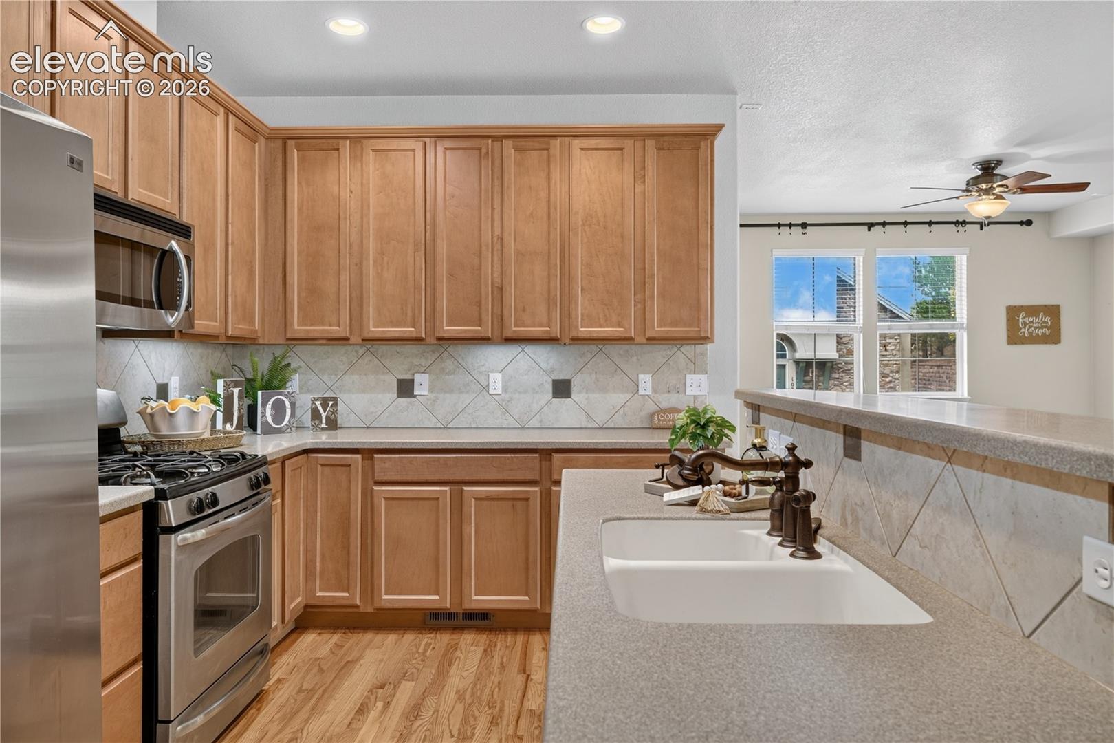Kitchen featuring wood cabinetry, stainless steel appliances, dual-basin sink with a bronze-finish faucet, stone-composite countertops, and a classic tile backsplash 