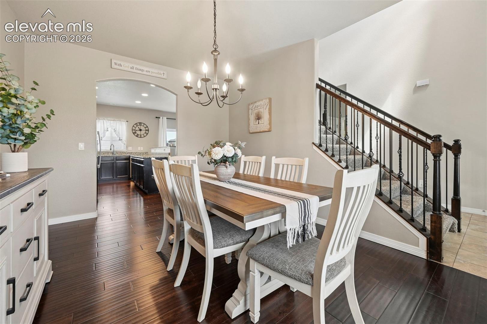 Rich wood-finish flooring, staircase with wrought iron balusters, arched entryway, and a hanging chandelier