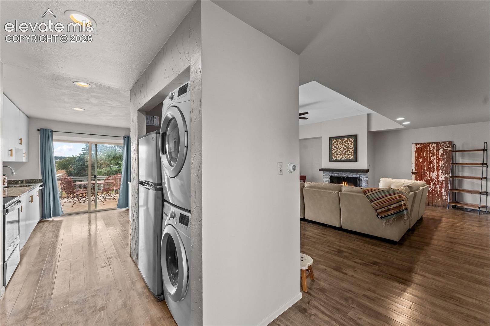 Kitchen featuring white cabinetry and stainless steel appliances, stacked laundry unit, wood-finish flooring, and recessed lighting