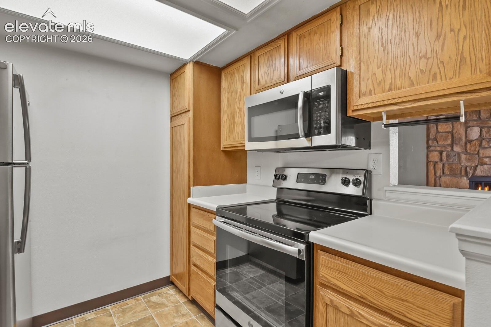 Kitchen featuring wood cabinetry, stainless steel GE microwave, GE stainless steel free standing oven/range with smooth glass top and linoleum flooring