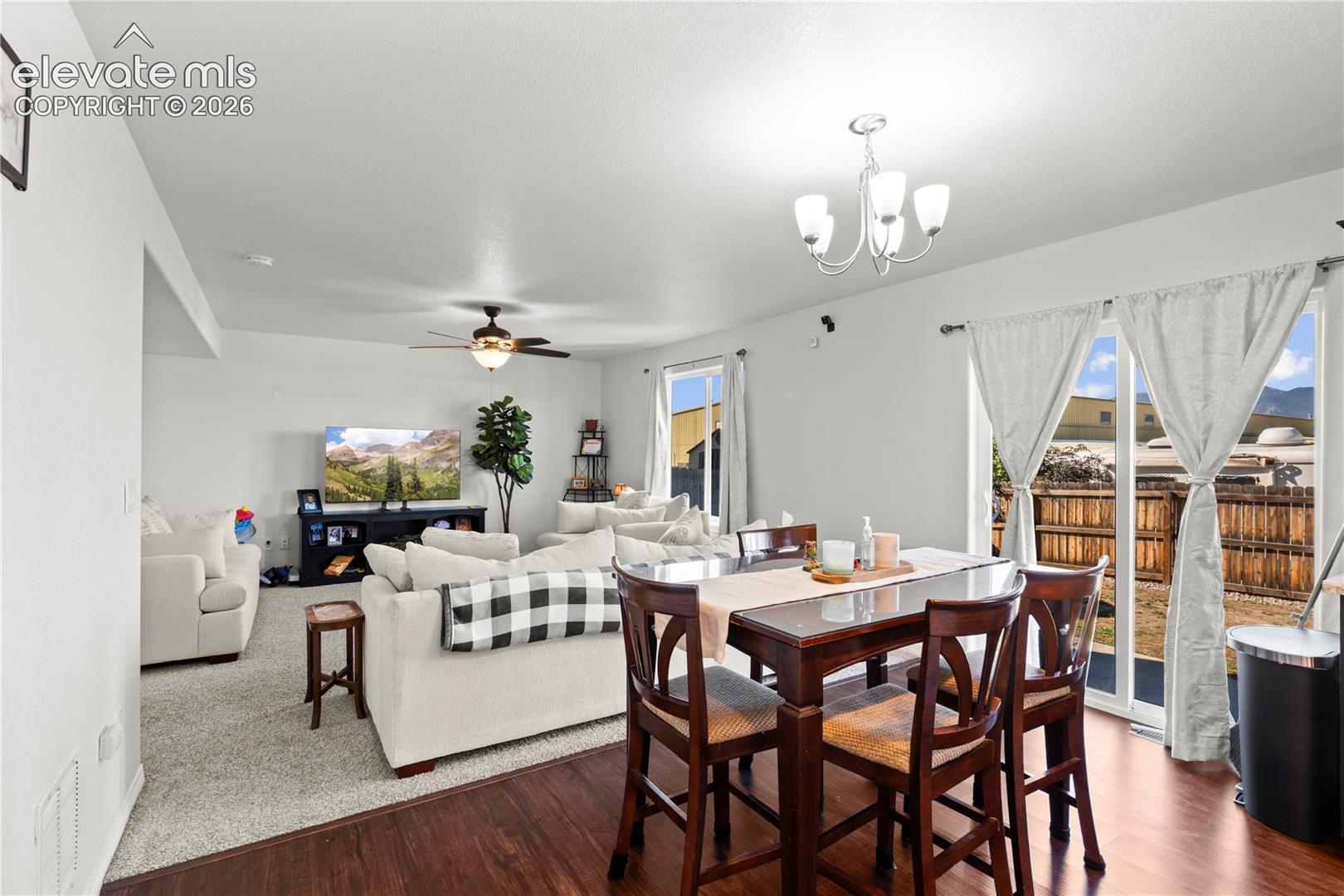 Open-concept area featuring wood-finish flooring, neutral carpeting, a multi-light chandelier, a ceiling fan, and sliding glass doors