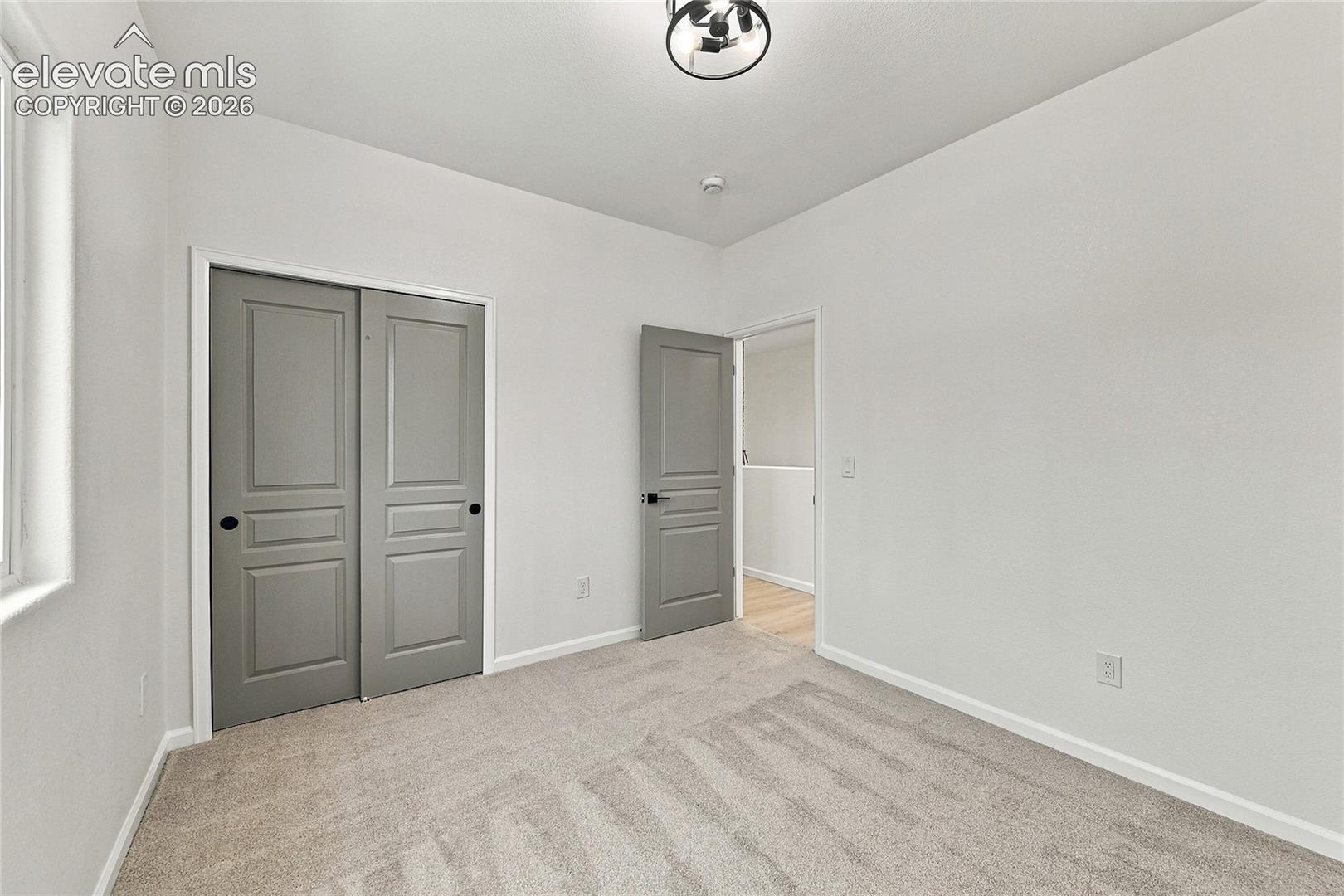 Neutral-toned wall-to-wall carpeting, grey shaker-style paneled doors, matte black hardware, and a modern circular flush-mount ceiling fixture