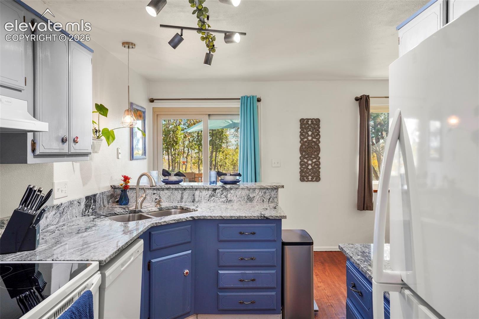 Kitchen featuring stone-finish countertops, stainless steel dual-basin sink with a gooseneck faucet, blue cabinetry, wood-finish flooring, and multi-directional track lighting