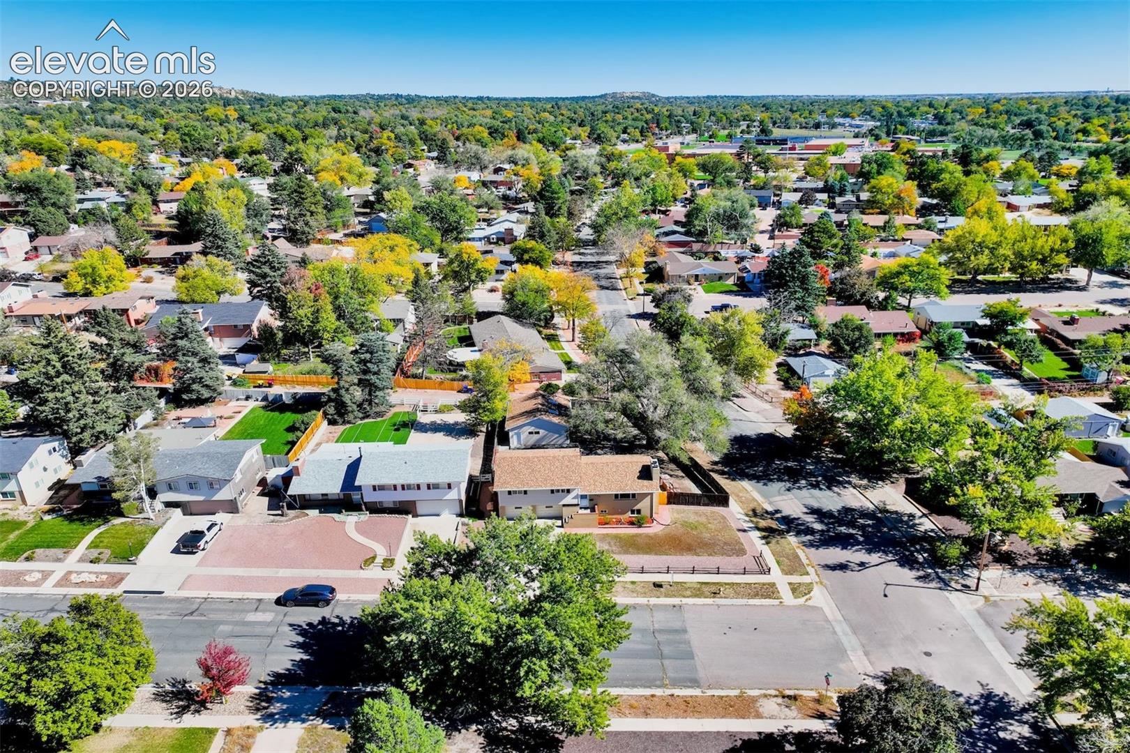 Aerial perspective featuring a residential lot with mature trees, a multi-car driveway, and paved street access