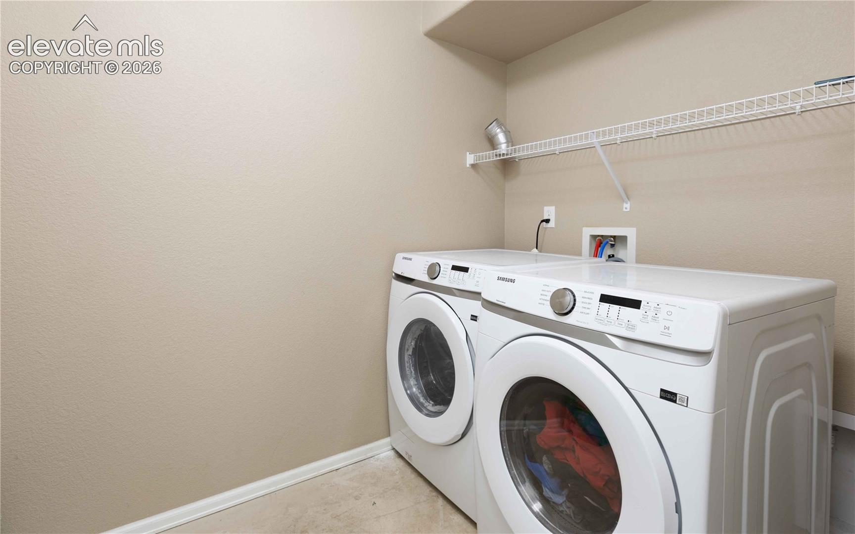 Laundry area featuring a high-mounted wire shelving unit, dedicated water hookups, and a recessed electrical outlet