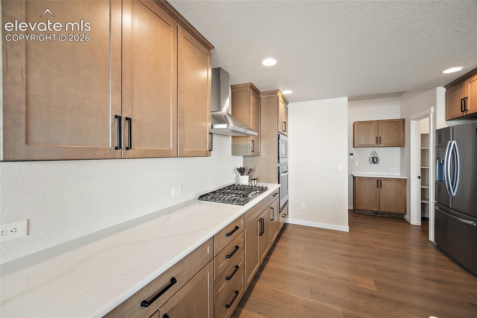 Kitchen featuring light wood-finish cabinetry with matte black hardware, white countertops, built-in stainless steel appliances, and wood-finish flooring