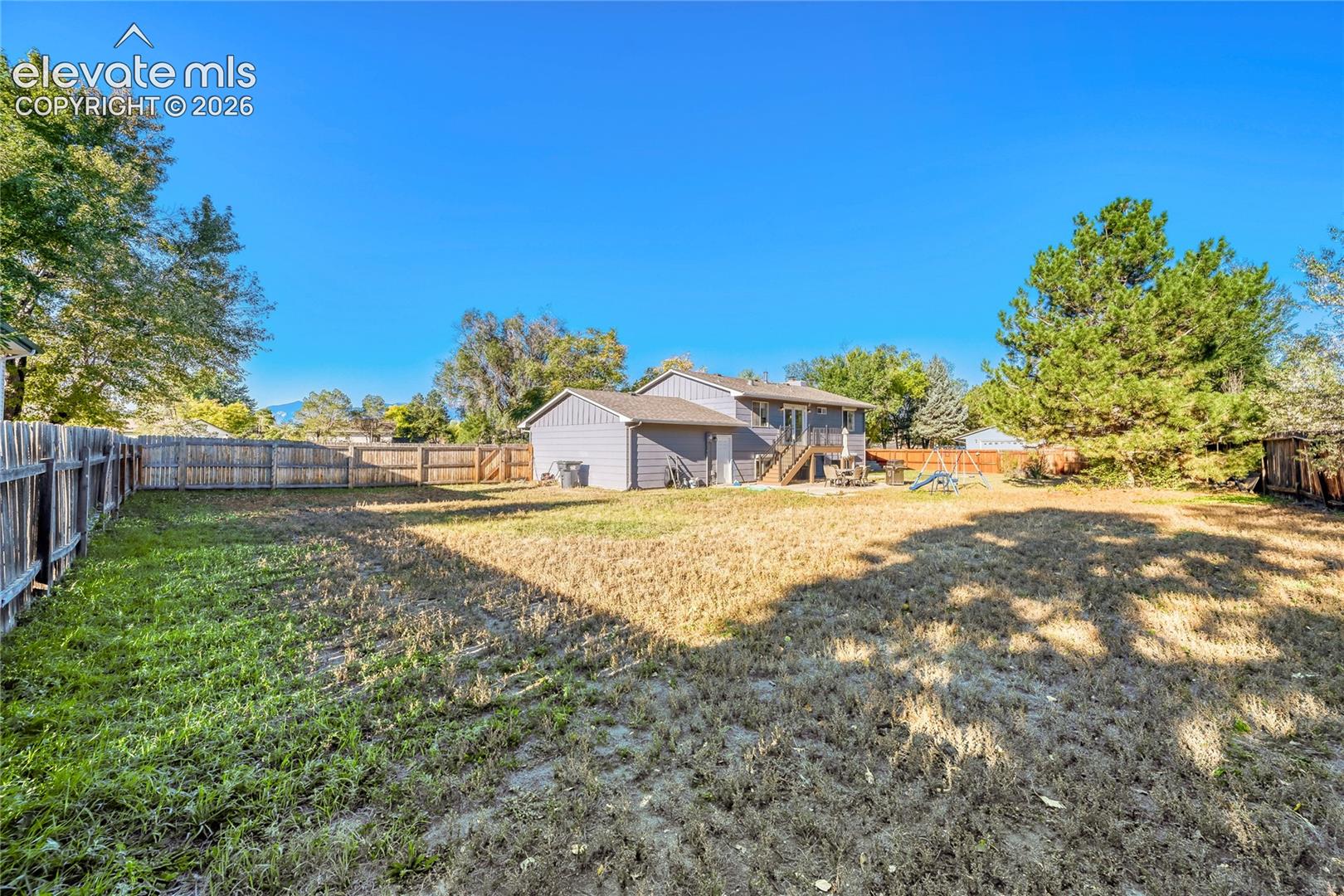 Expansive backyard featuring a wood-panel fence, mature trees, and an elevated rear deck
