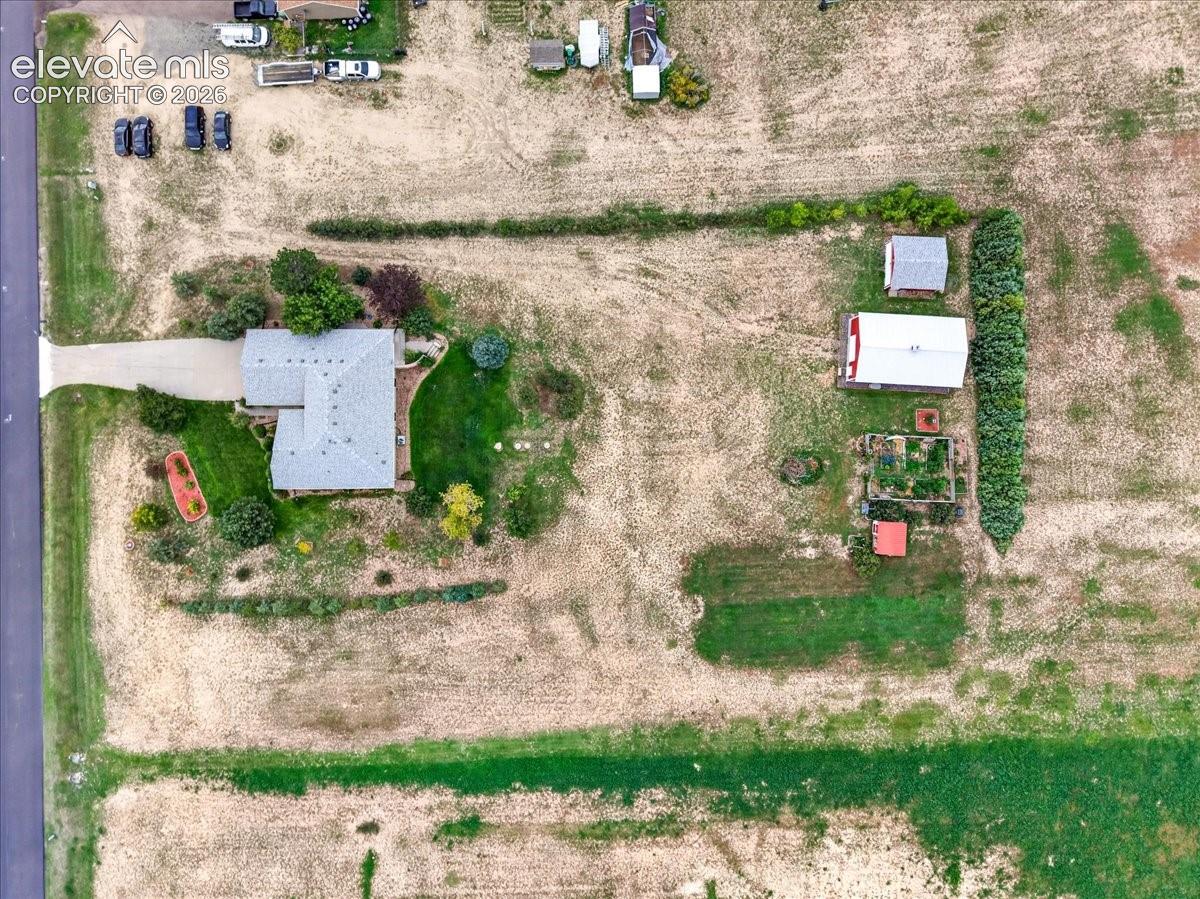 Aerial view of expansive lot featuring a single-story residence, detached garage, established perimeter tree rows, and cultivated garden areas