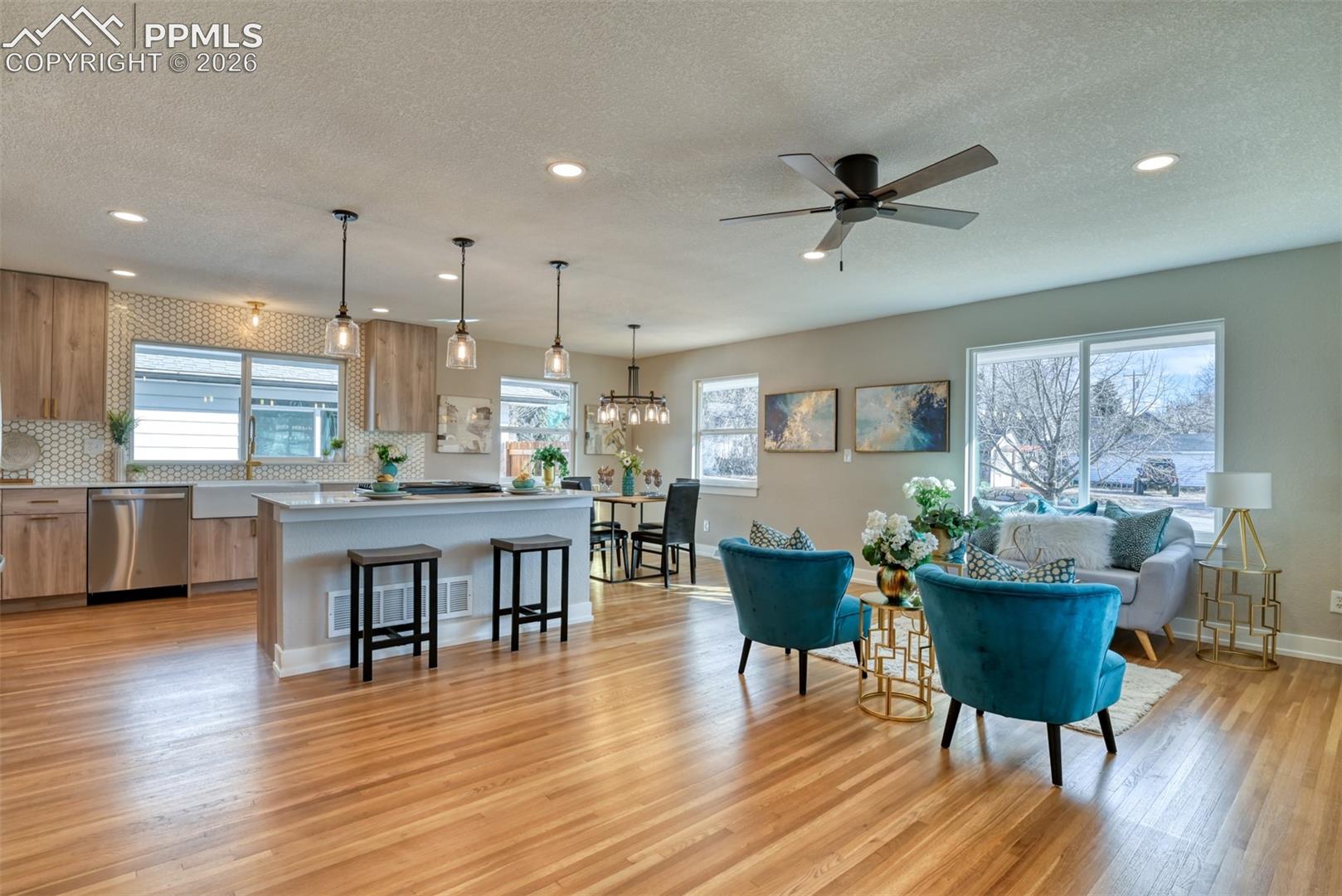 Living room featuring light wood-type flooring, ceiling fan, a textured ceiling, and hanging lights