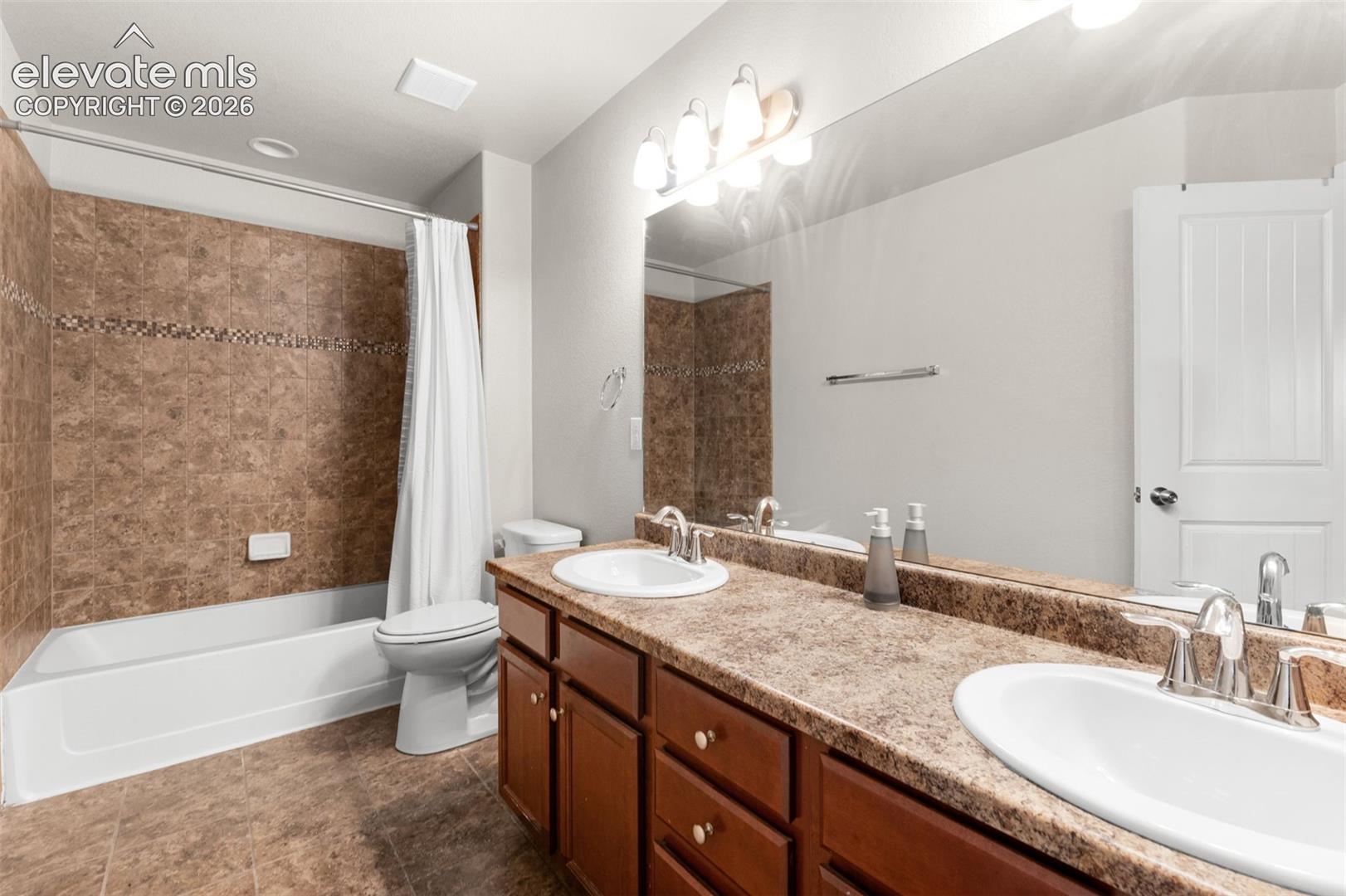 Bathroom featuring a dual-sink vanity with a stone-finish countertop, wood cabinetry, large vanity mirror, and a tub-shower combination with tile surround