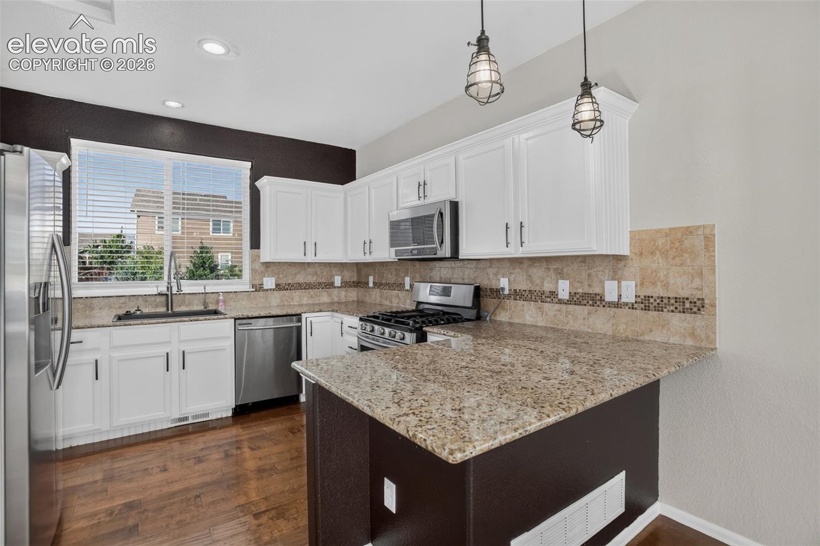 Kitchen featuring white cabinetry, stainless steel appliances, granite countertops, tile backsplash with mosaic accents, and wood-finish flooring