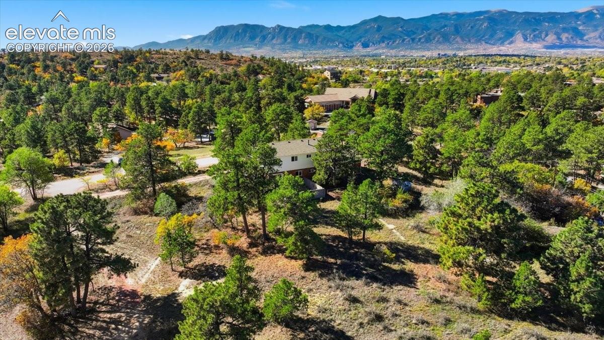 Aerial perspective of a multi-level residence situated on a wooded lot featuring mature pine trees, native vegetation, and a mountainous backdrop