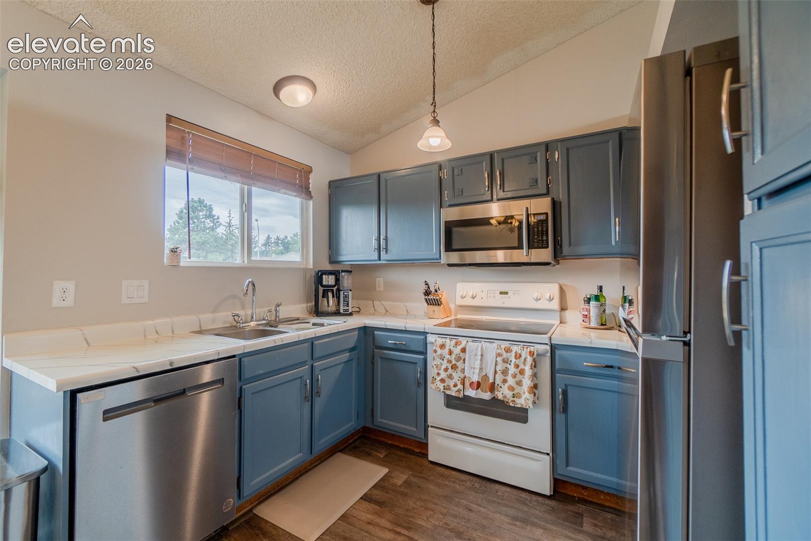 Kitchen featuring blue cabinetry, white countertops, stainless steel dishwasher, stainless steel microwave, and wood-finish flooring