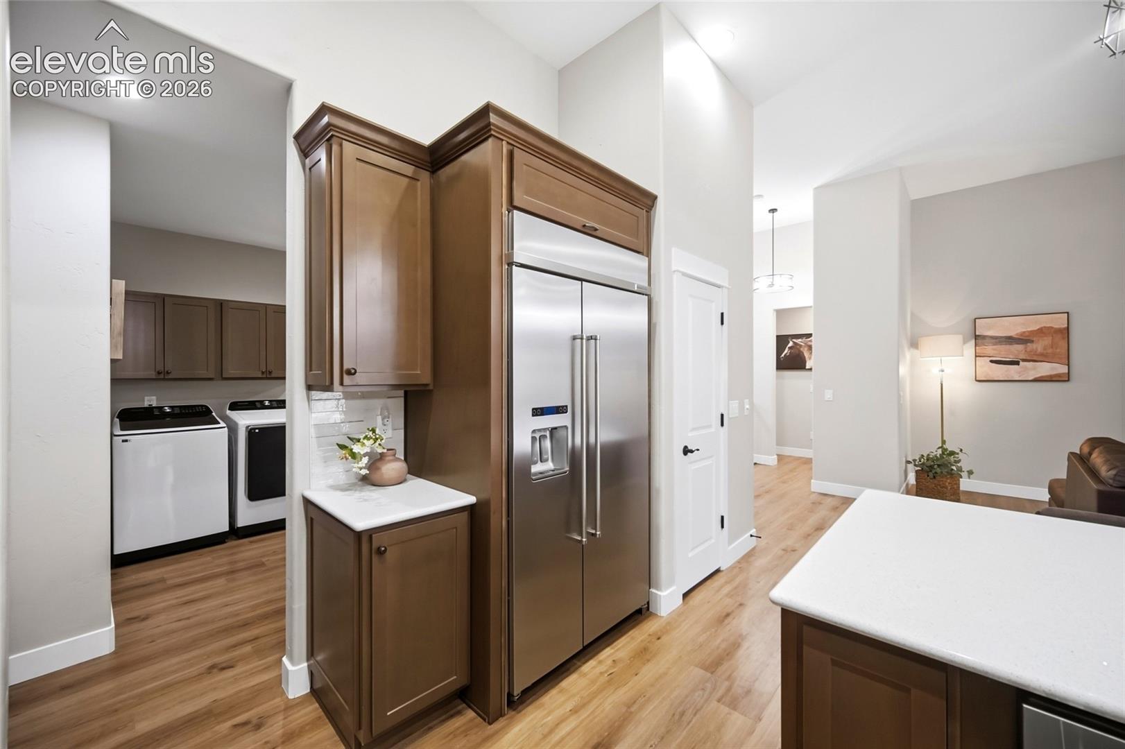 Wood-finish flooring, full-height built-in cabinetry with stainless steel refrigerator, white solid-surface countertops, and recessed ceiling lighting