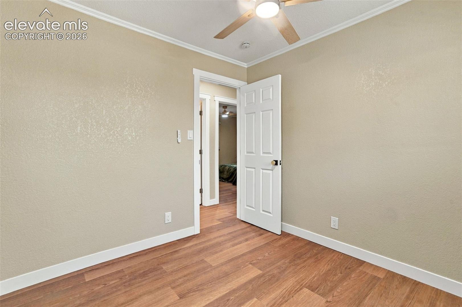 Neutral-toned interior featuring wood-finish flooring, a six-panel door, and a ceiling fan with integrated lighting