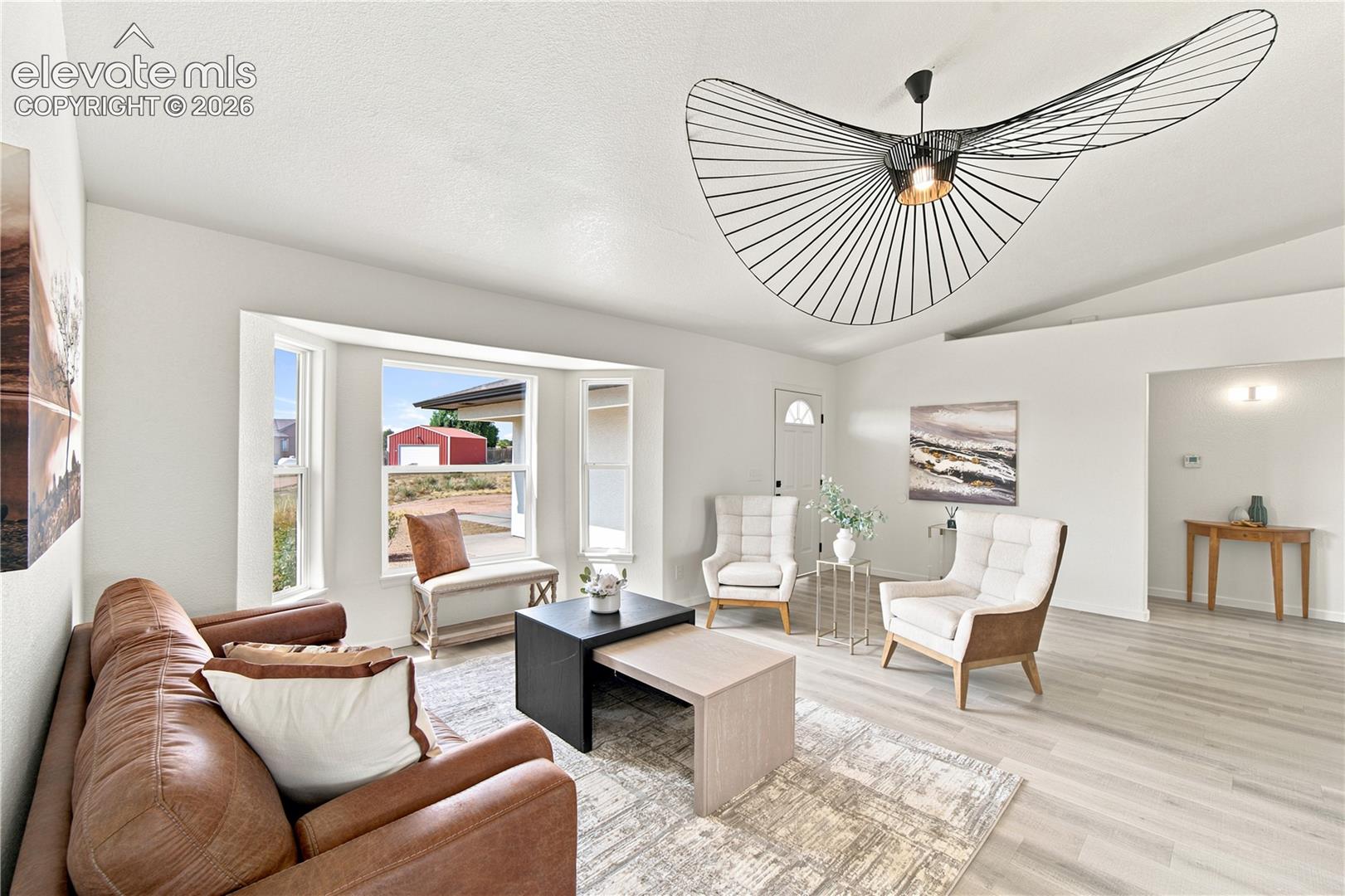 Spacious living area featuring light wood-finish flooring, a contemporary ceiling light fixture, a bay window, and white painted walls