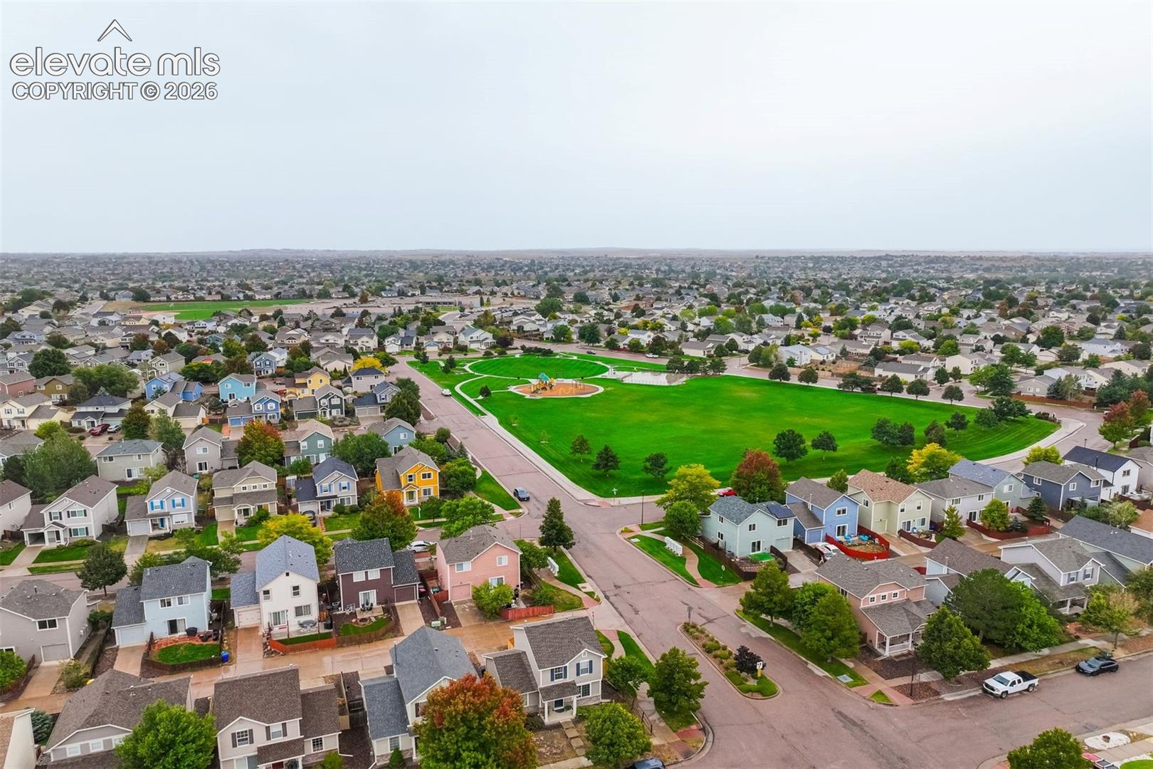 Expansive green space featuring playground equipment, surrounded by residential properties and mature trees
