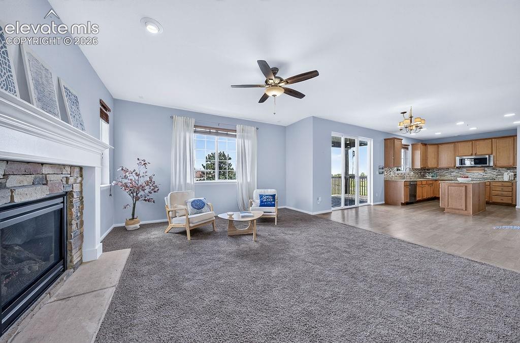 Open-concept living space featuring a stacked stone fireplace with a white mantel, kitchen with wood cabinetry and a center island, and glass sliding doors