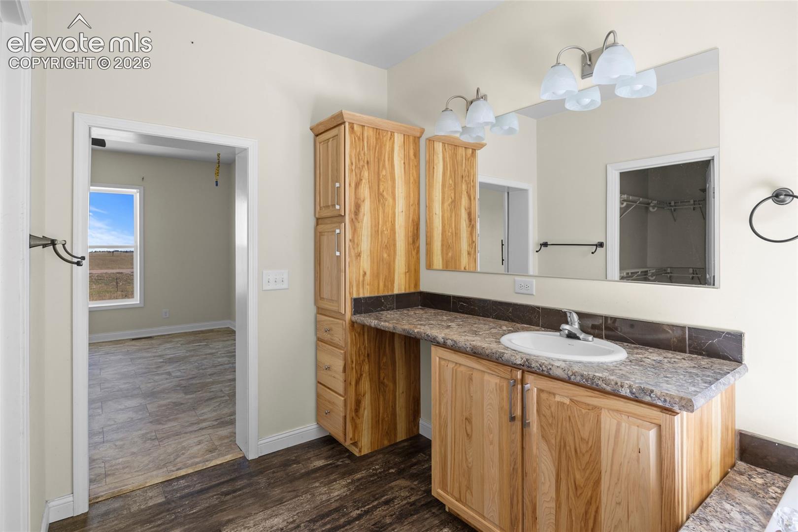 Bathroom featuring wood cabinetry, integrated storage tower, stone-patterned countertop, oval drop-in sink, and full-width vanity mirror