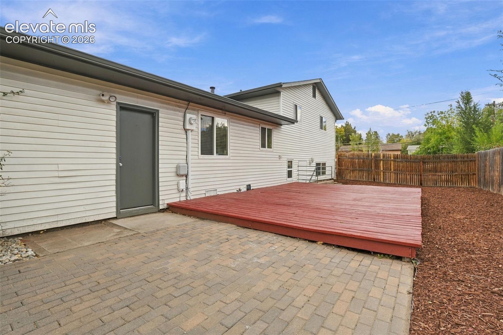 Exterior area featuring a raised wood-finish deck, paver stone patio, horizontal siding, and perimeter wood fencing