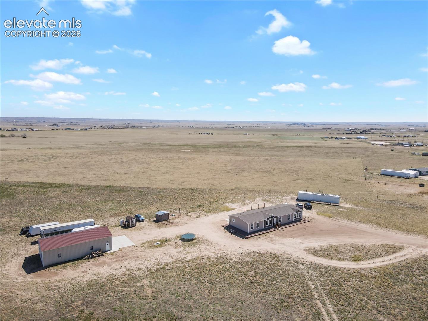 Aerial perspective featuring a multi-structure property on expansive acreage, including a detached workshop with a metal roof and a gravel access drive