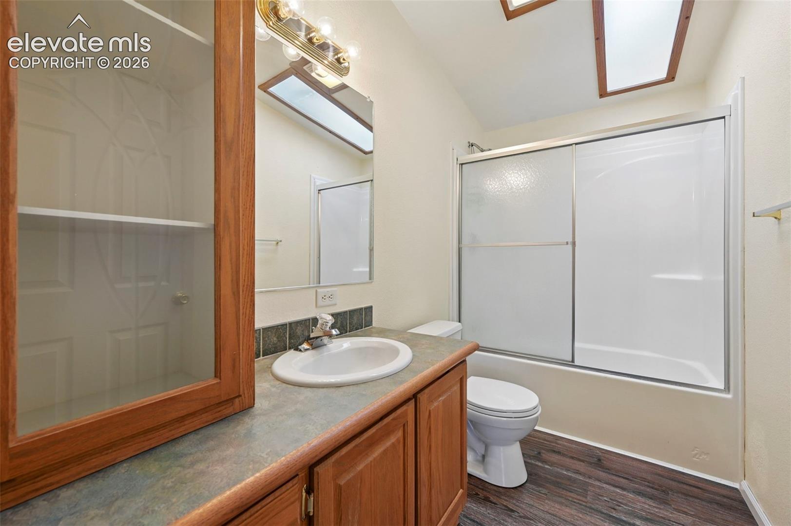 Bathroom featuring wood-finish cabinetry, built-in display shelving, skylights, tub-shower combination with sliding doors, and wood-finish flooring