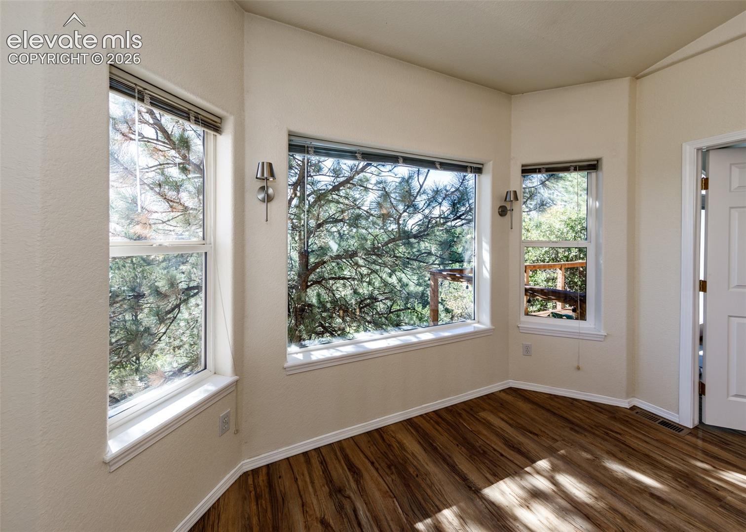 Bay window configuration with three-pane glazing, wood-finish flooring, and wall-mounted metallic sconce lighting