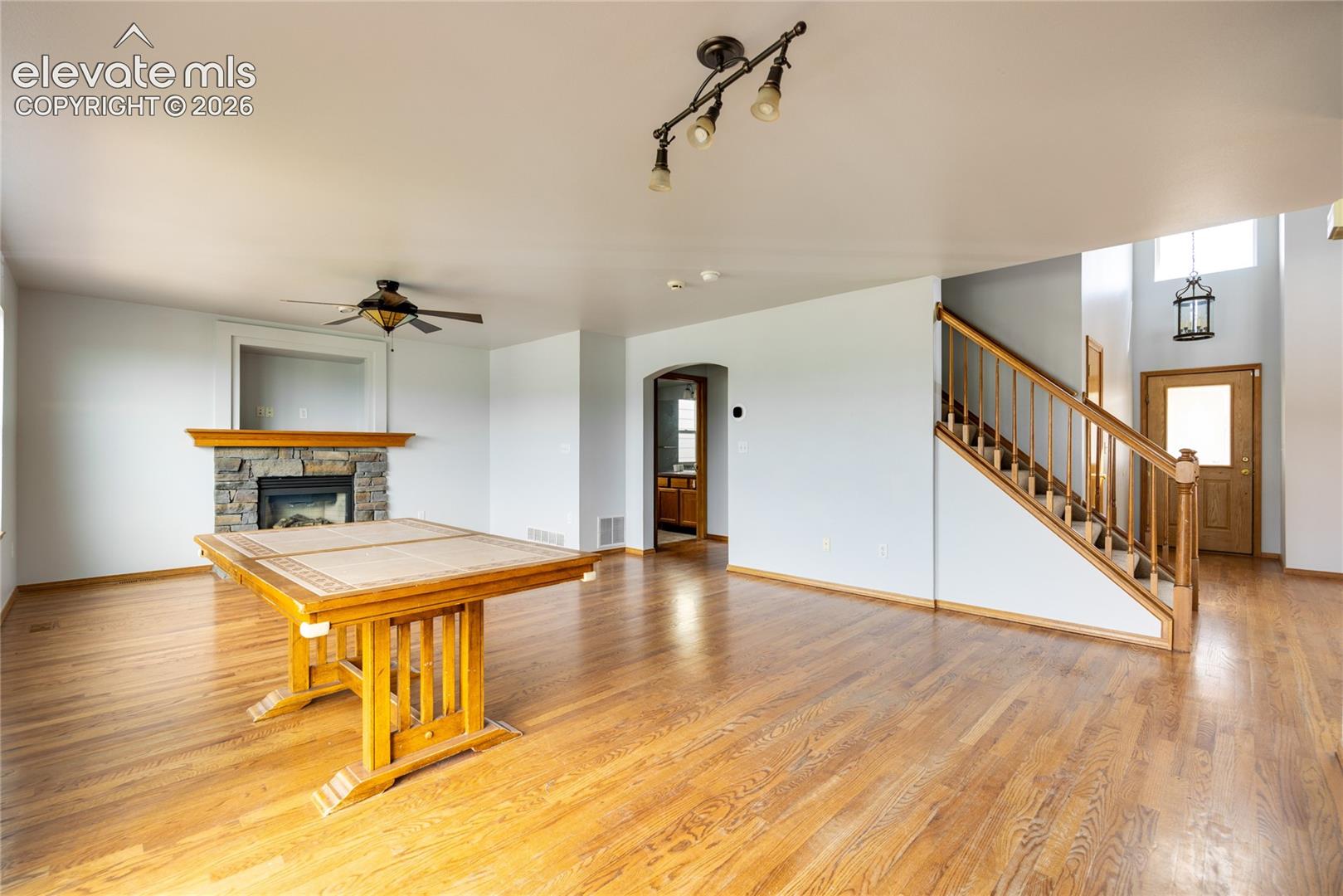 Hardwood flooring, stone-faced fireplace with wood mantel, built-in ceiling fan, wood staircase with balusters, and a front entry door with transom window