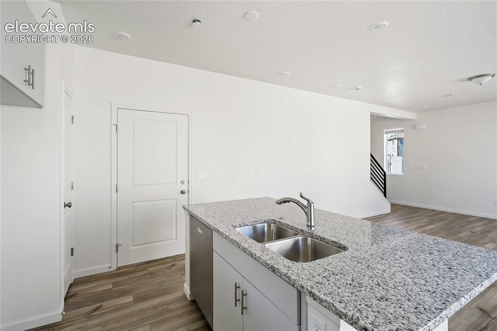 Kitchen island with a dual basin sink and a high-arc faucet, granite countertop, recessed lighting, and wood-finish flooring
*photos of a model home*