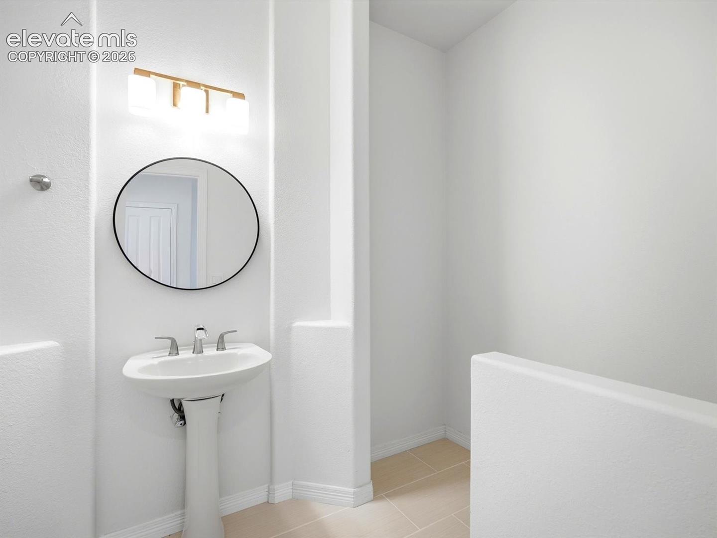 Pedestal sink with a polished metal faucet, round wall-mounted mirror, and three-light fixture with frosted glass shades