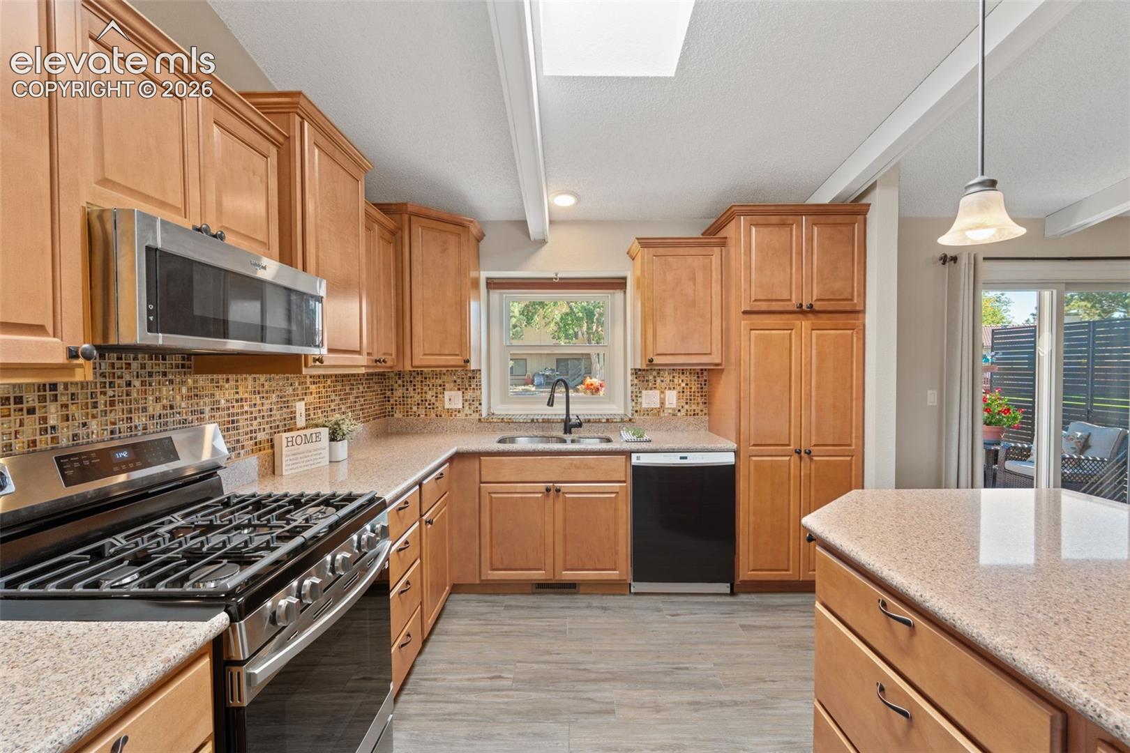 Kitchen featuring wood cabinetry, solid surface countertops, mosaic tile backsplash, stainless steel appliances, and wood-finish flooring