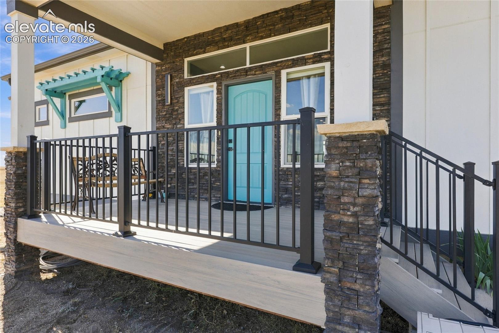 Covered front porch featuring stacked stone accents, wood-finish decking, black metal railings, a teal entry door, and a decorative turquoise window awning