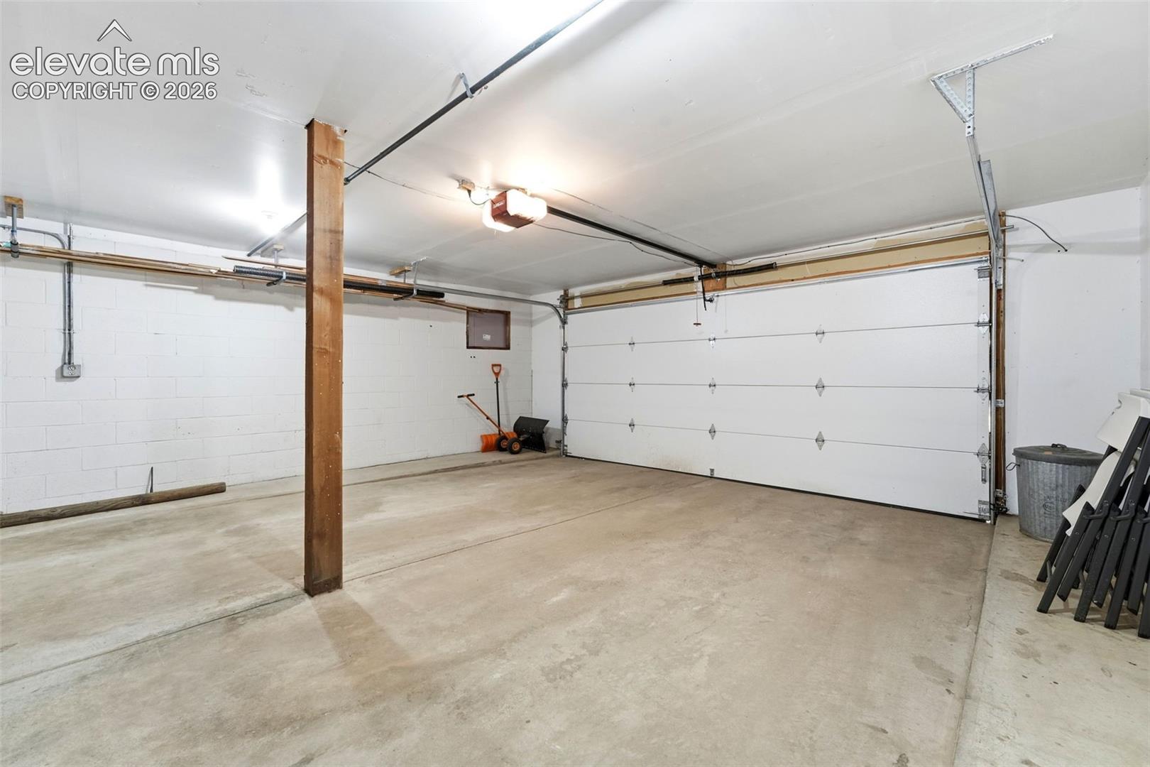 Concrete flooring with a white paneled garage door and a ceiling-mounted garage door opener