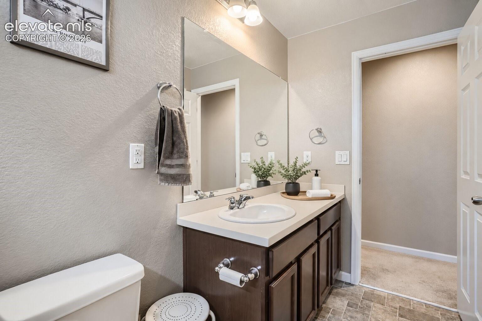 Bathroom featuring a vanity with dark-finish cabinetry, a solid-surface countertop, an integrated porcelain sink, a full-width vanity mirror, and tile flooring