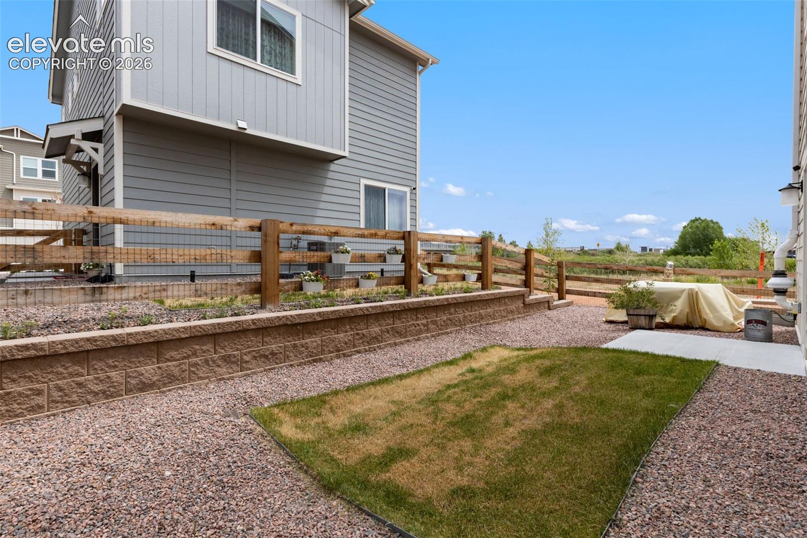 Tiered backyard featuring a retaining wall, a split-rail fence, and gravel landscaping