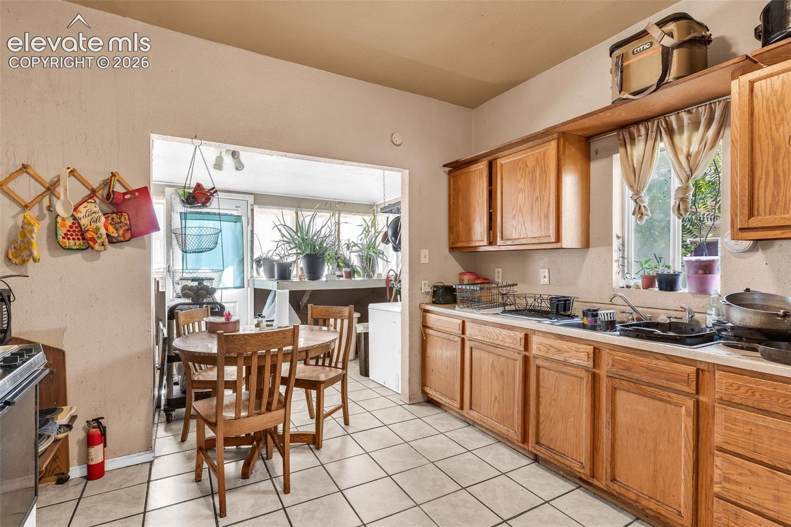 Kitchen featuring extensive wood-finish cabinetry, white tiled flooring, and a window above the sink