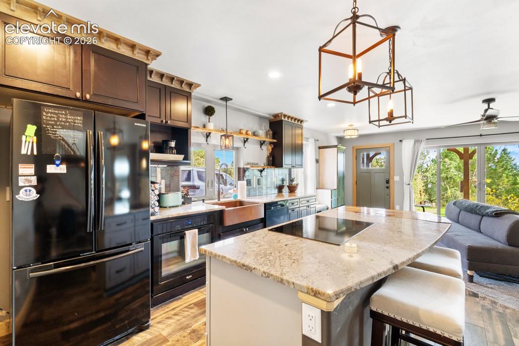 Kitchen featuring wood-finish flooring, dark wood cabinetry, granite countertops, and a copper-toned farmhouse sink