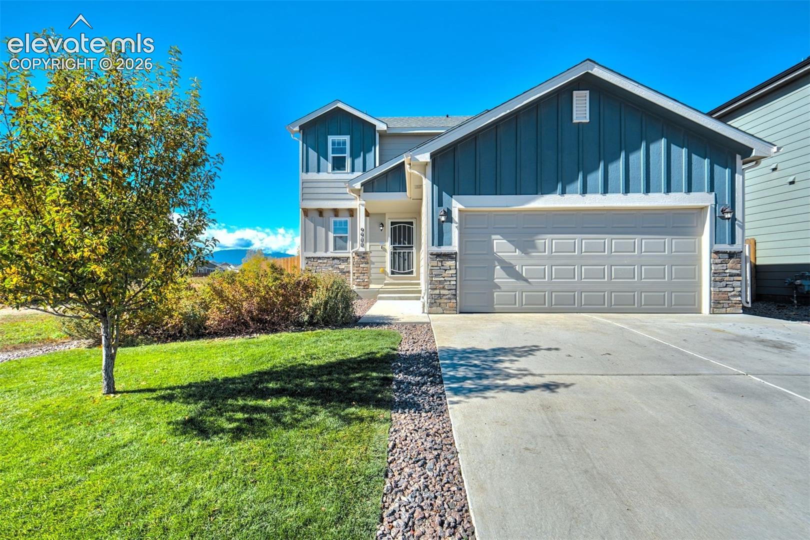Two-story exterior featuring blue vertical siding, stone veneer accents, concrete driveway, and covered entryway