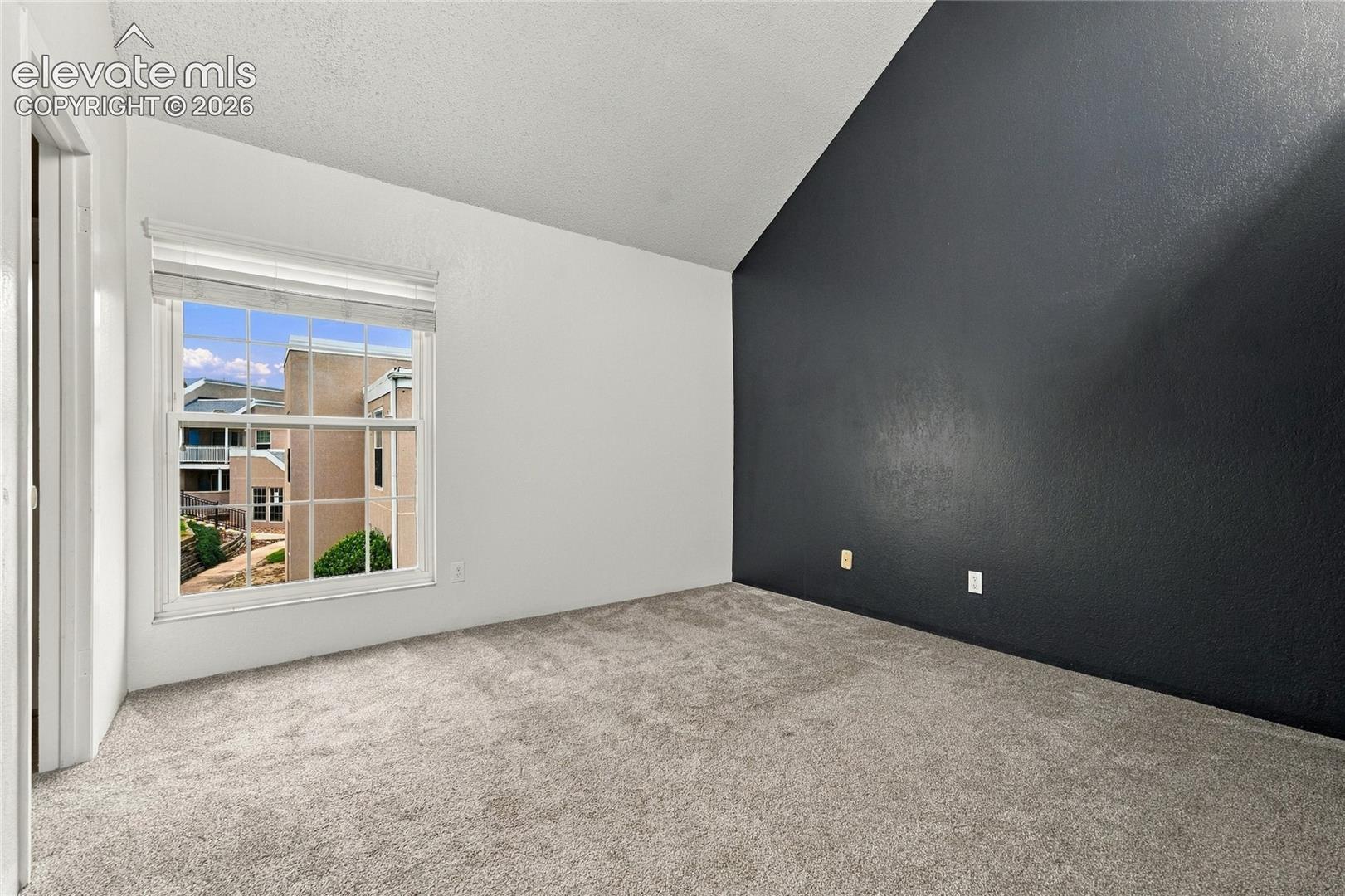 Vaulted ceiling with a contrasting dark accent wall, neutral carpeting, and a multi-pane window