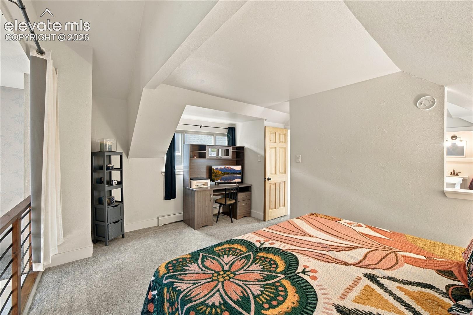 Vaulted ceilings with architectural angles, carpeted flooring, window with natural light, and natural wood door with brass hardware