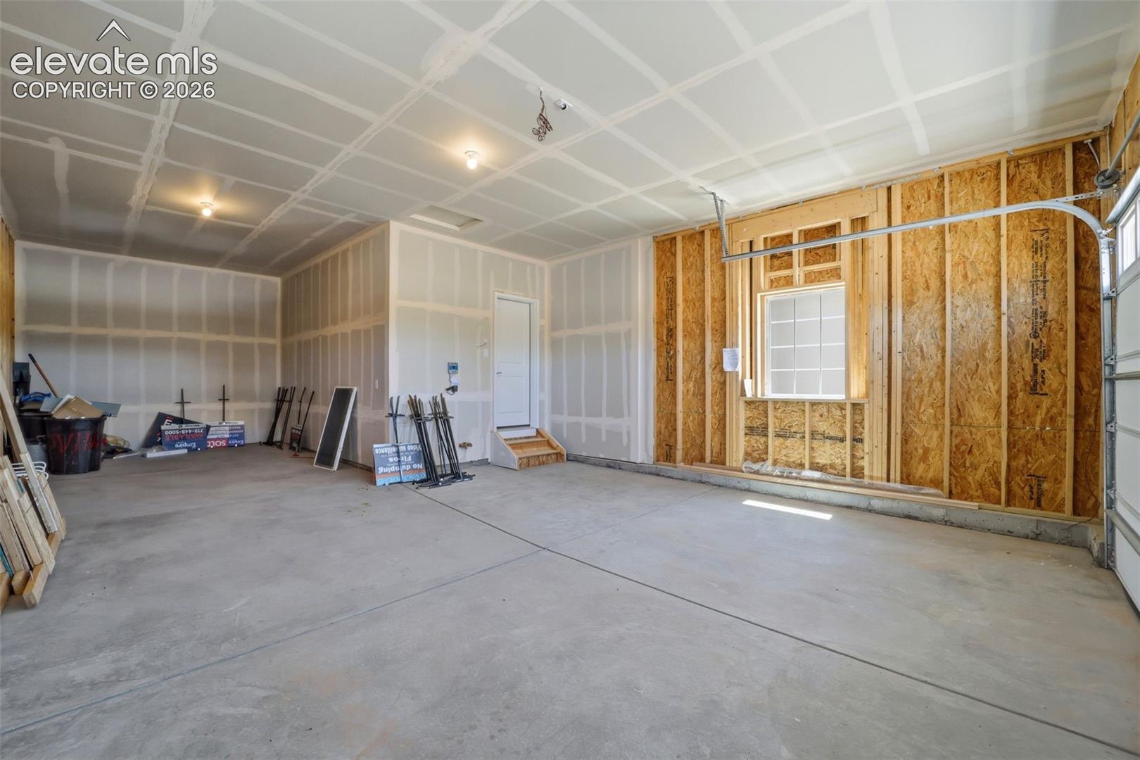 Multi-vehicle garage featuring concrete flooring, drywall-finished ceiling, exposed wood-frame wall, single-pane window, and overhead door hardware