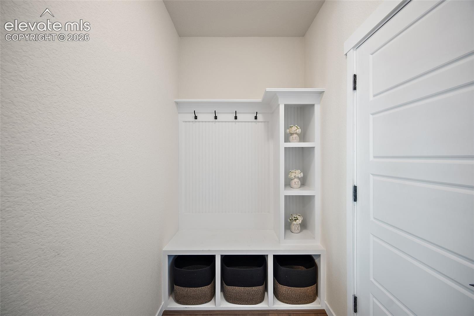 Built-in white storage unit with cubbies, upper shelving, and dark-finish coat hooks
